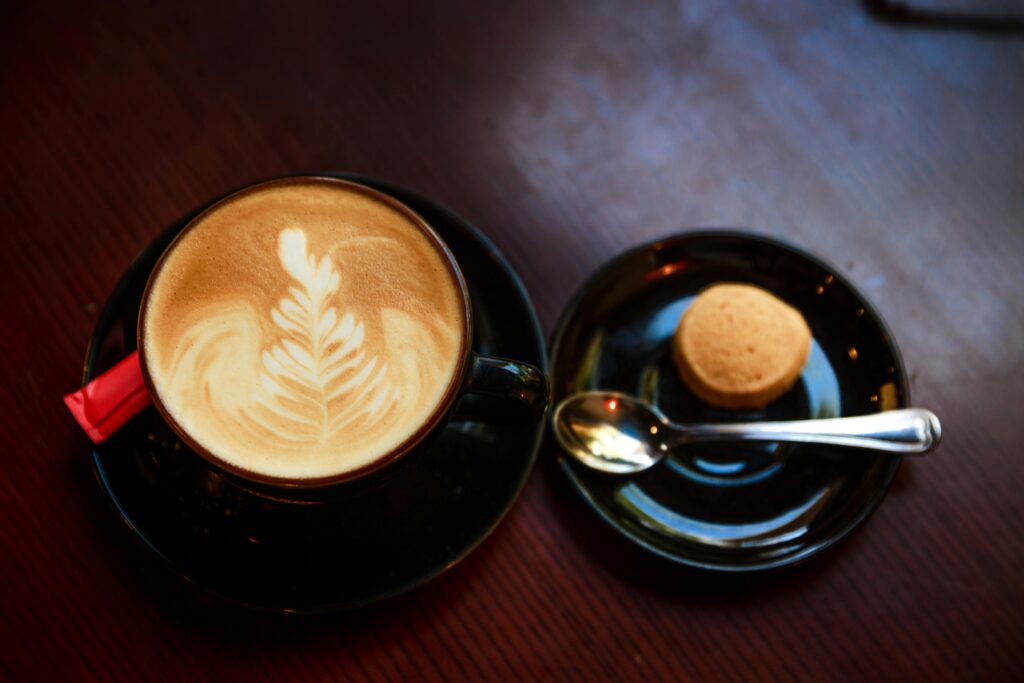 pexels-photo-2133535-2133535 A beautifully crafted cappuccino with latte art, accompanied by a small cookie on a dark wooden table.