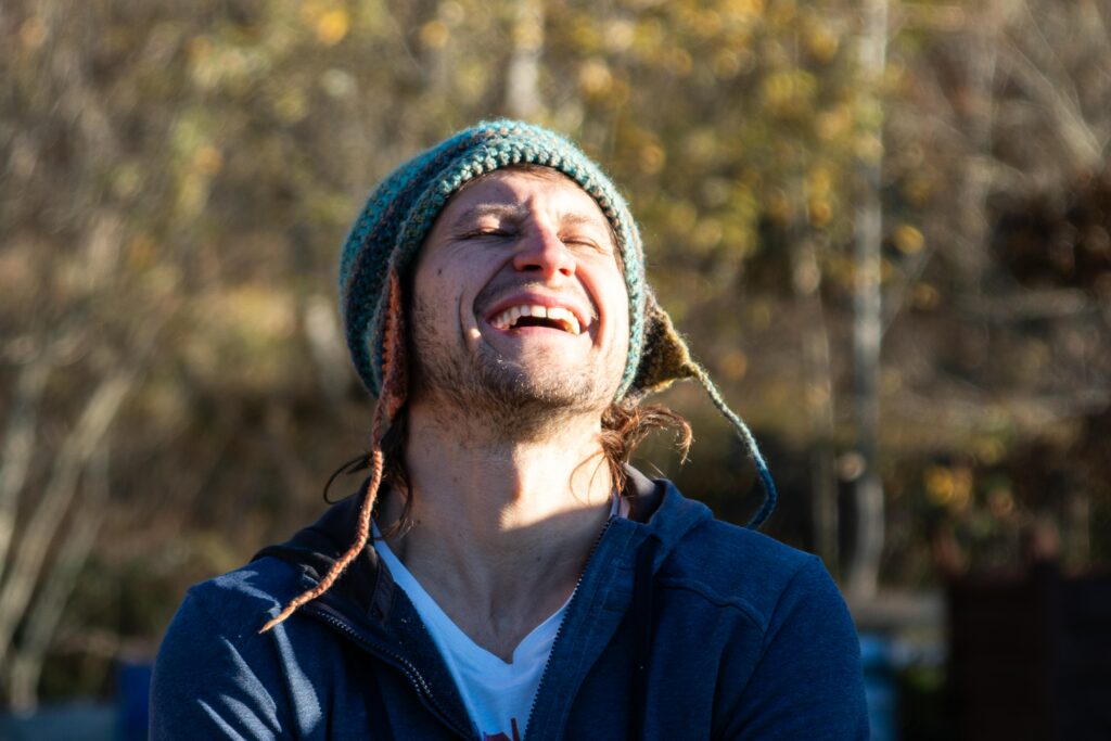 pexels-photo-28232845-28232845 A joyful man in a knit hat laughs under the sun in a park setting during fall.