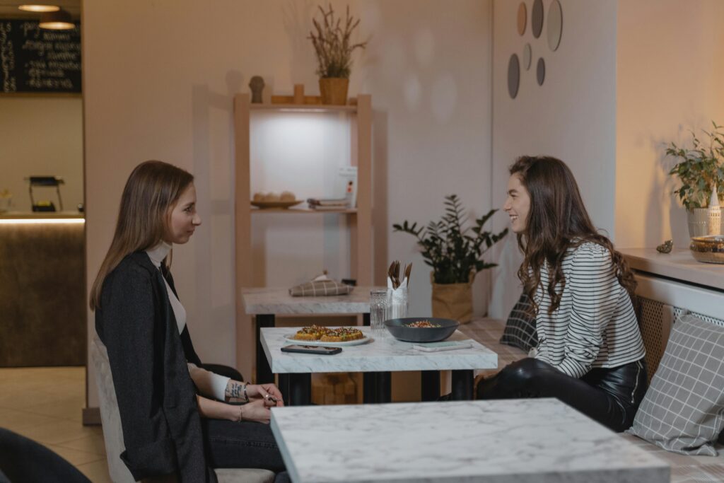 pexels-photo-6327151-6327151 Two women enjoying a conversation over a meal at a cozy indoor cafe setting.